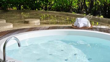 Un jacuzzi con cubierta de madera, rodeado de abundante vegetación.