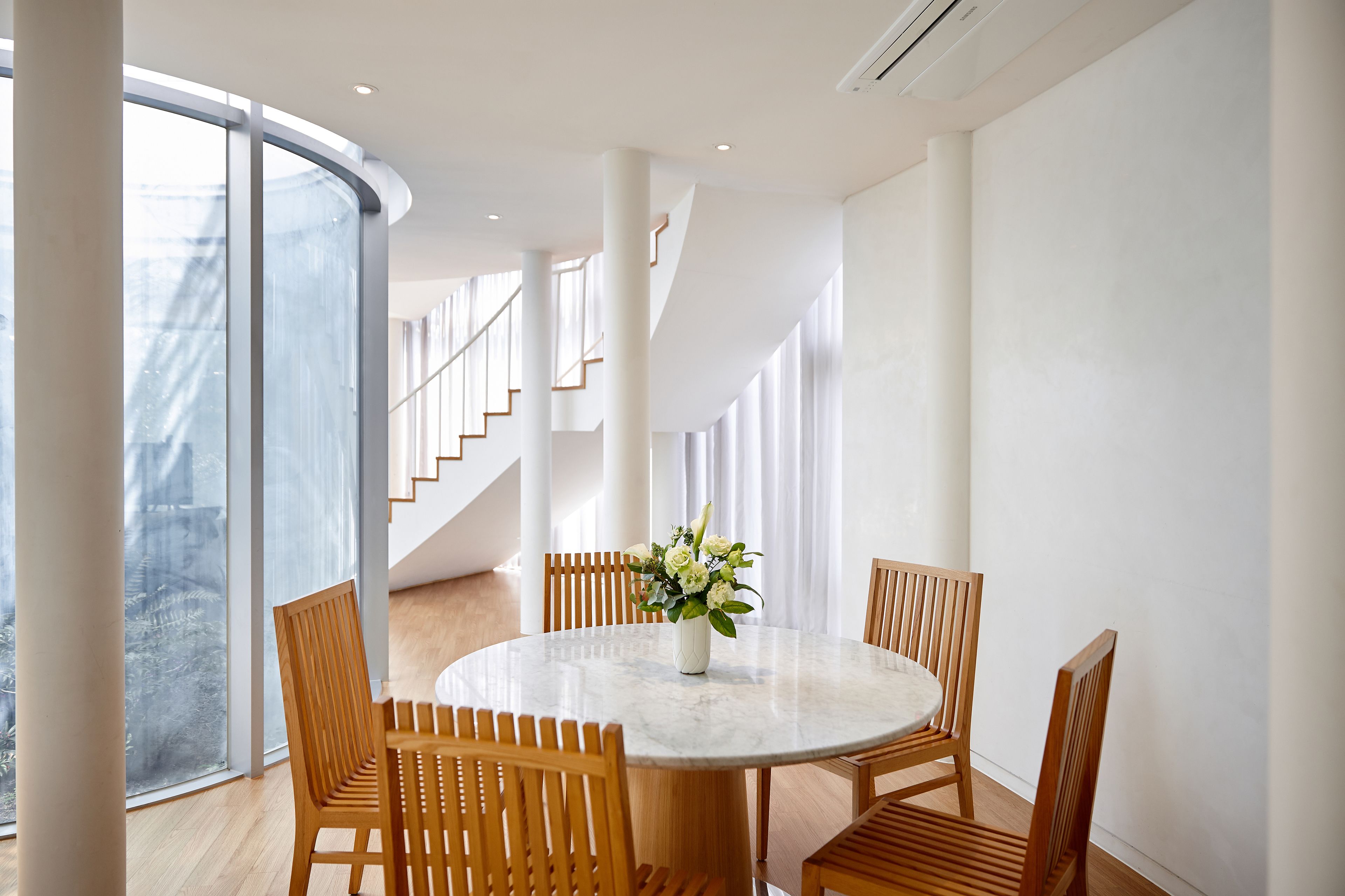 A modern dining area with a round table, wooden chairs, and a vase of flowers.