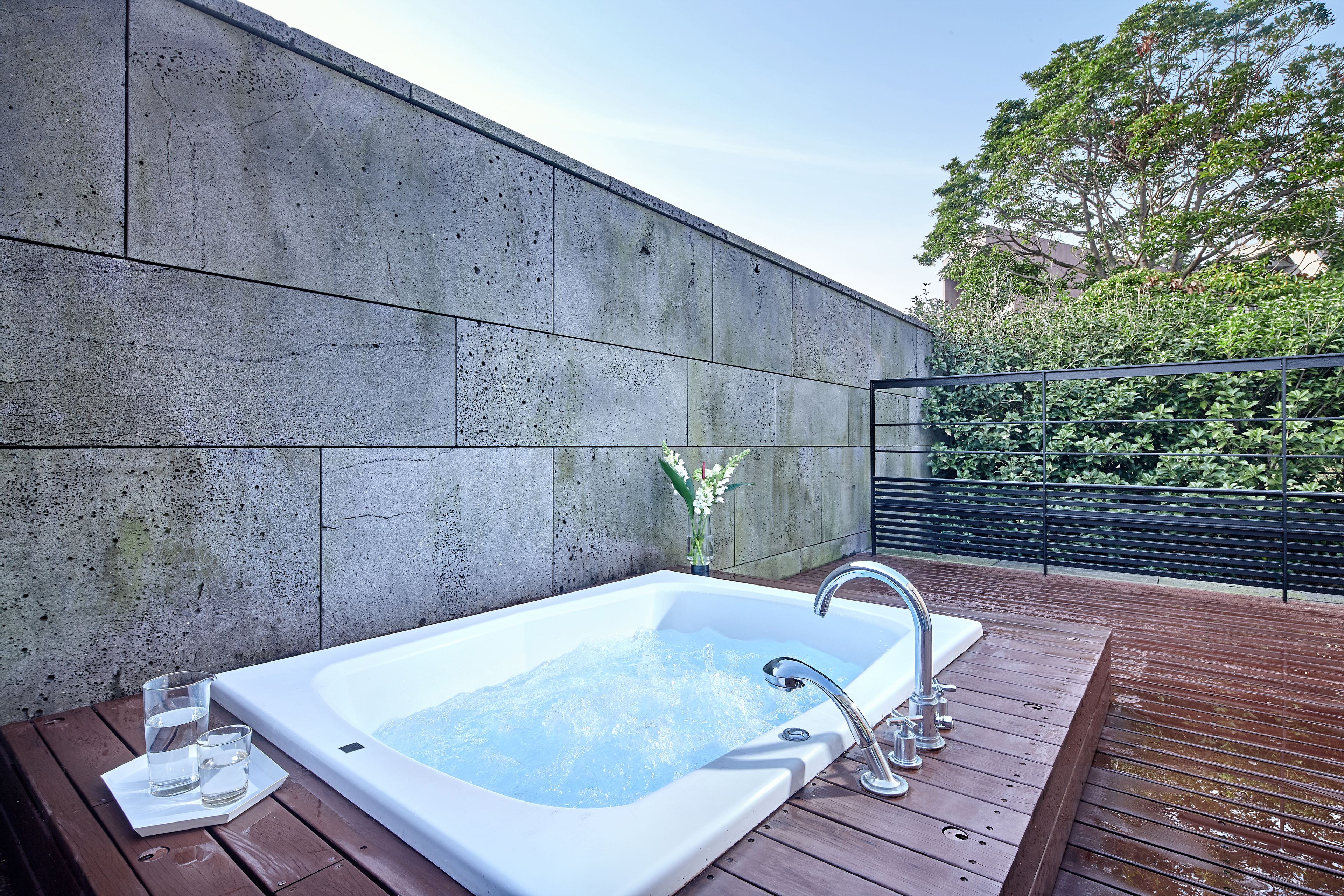 Un área de spa con hidromasaje, terraza de madera y pared de hormigón.