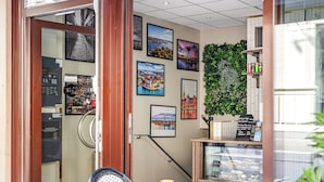 Um café com porta de vidro, quadros nas paredes, uma pequena mesa com vela e uma vitrine com doces.