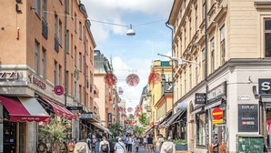 Rua com lojas e restaurantes, incluindo um hotel visível.