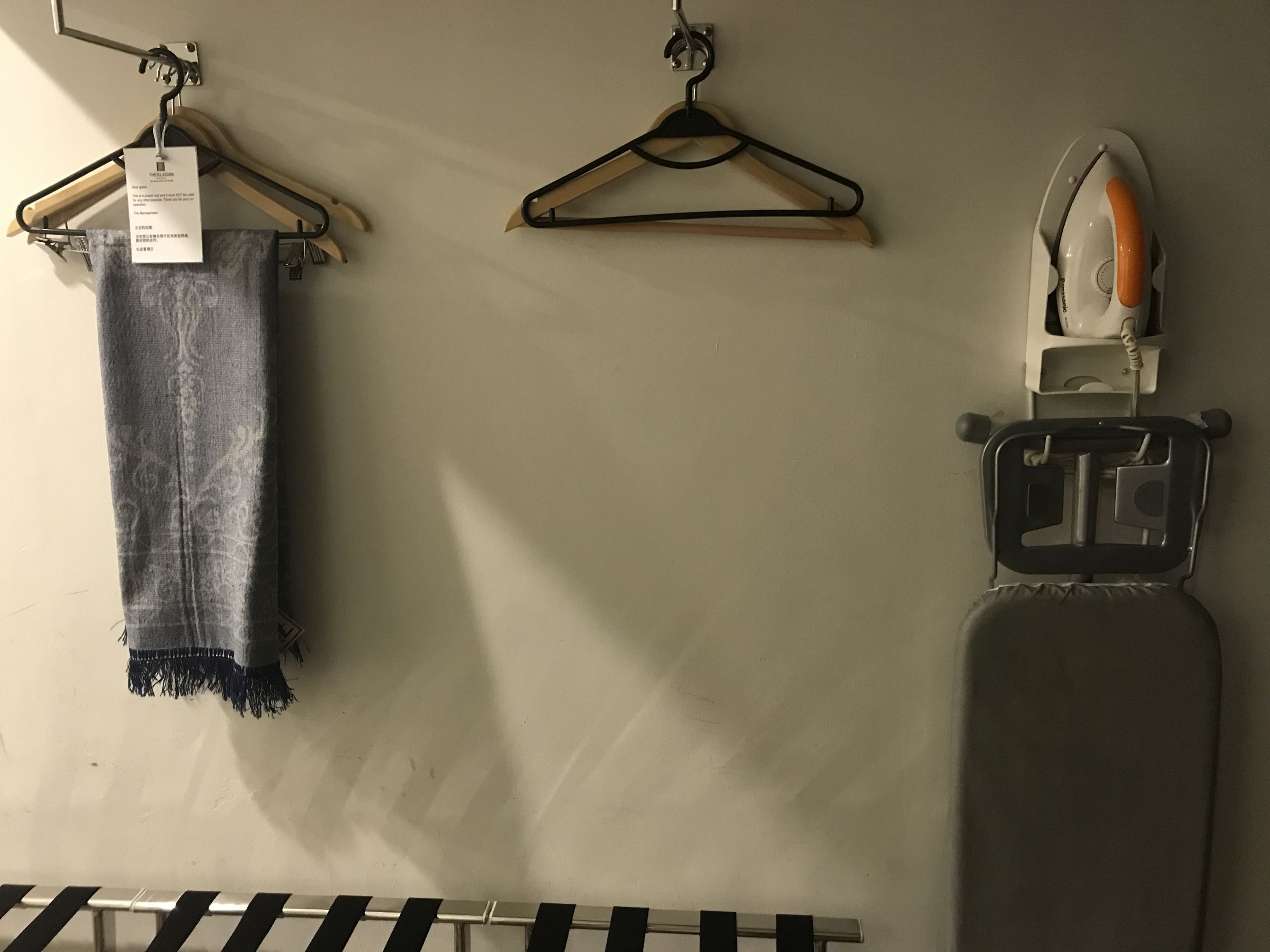 A wall-mounted ironing board with an iron, a wooden hanger with a tag, and a metal rack with hangers.