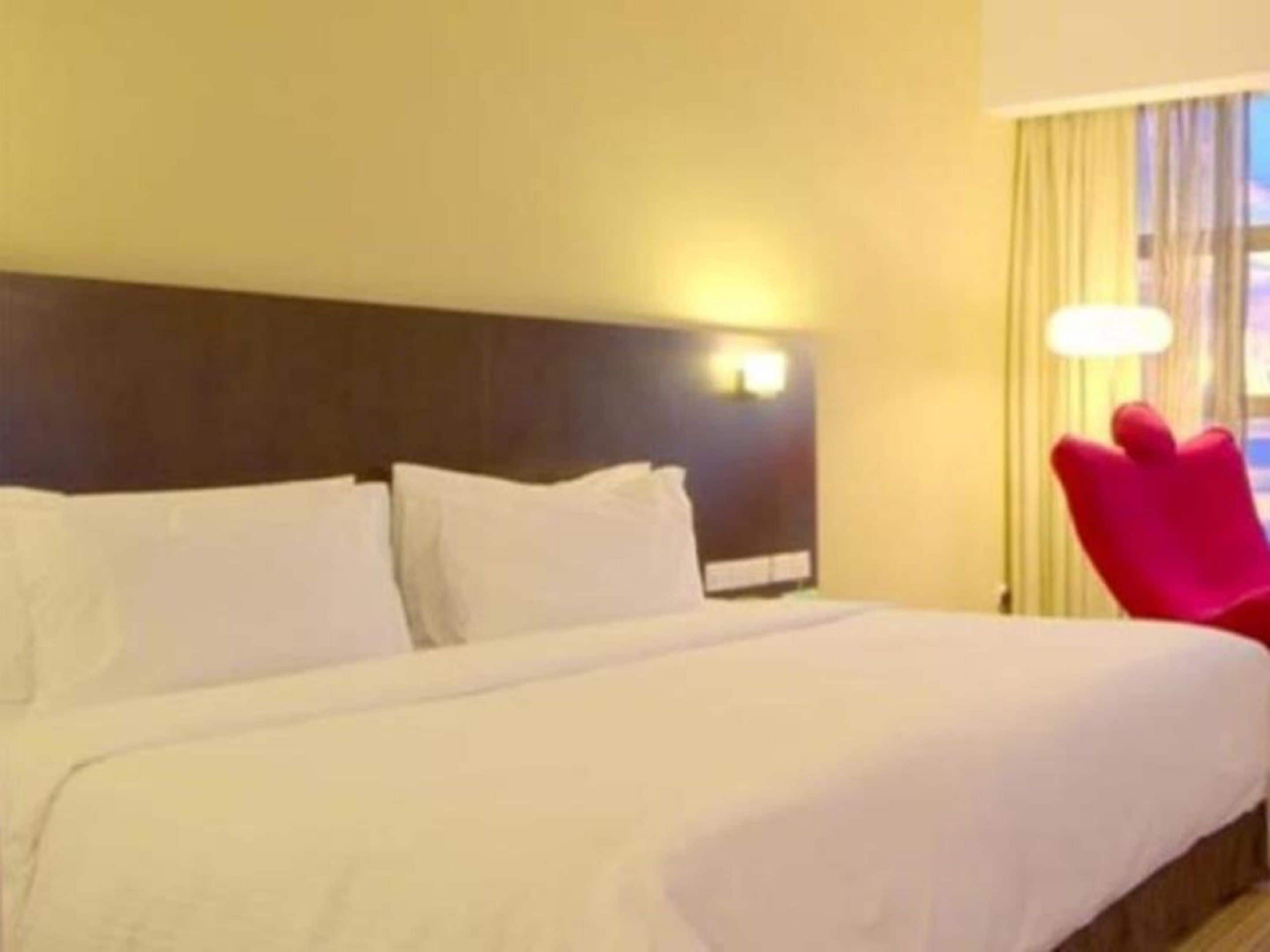 Una habitación de hotel con una cama grande, un cabecero con una lámpara y una silla roja.