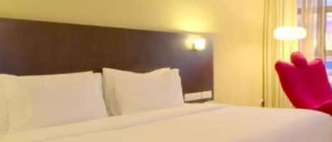 Una habitación de hotel con una cama grande, un cabecero con una lámpara y una silla roja.