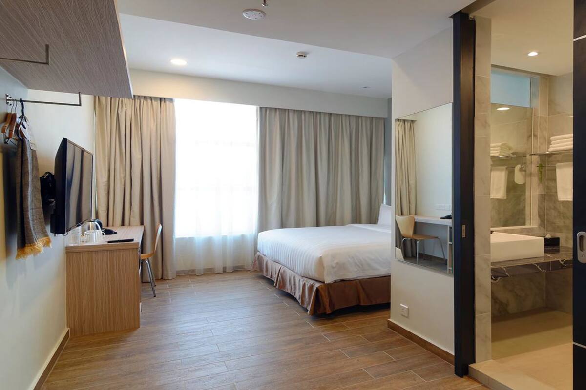 A hotel room with a bed, a desk, a chair, a TV, a bathroom with a shower and a bathtub.