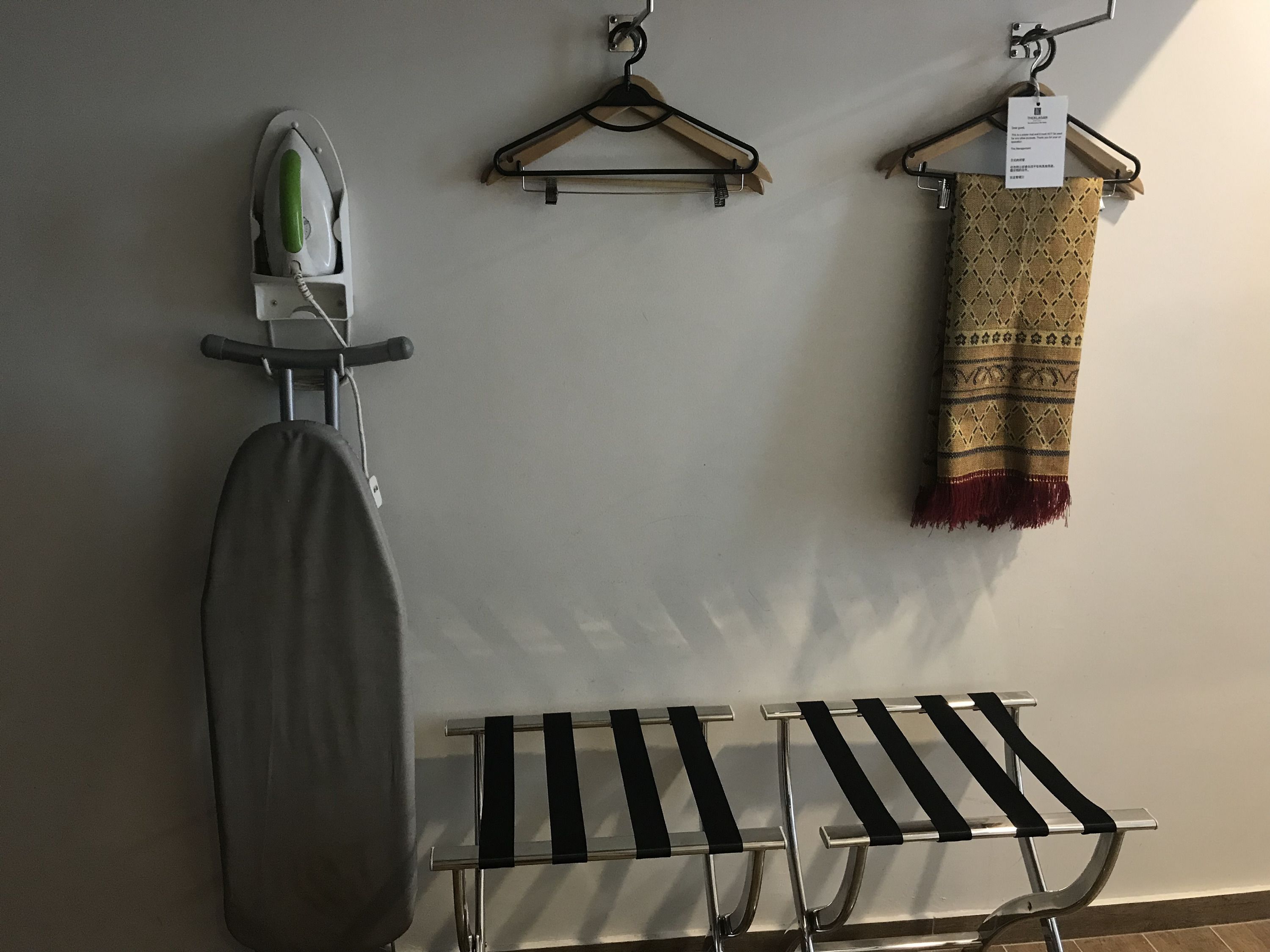 A wall-mounted ironing board with an iron, a rack with hangers, and a patterned cloth on a hanger.