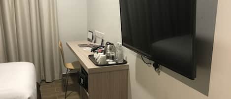 A hotel room with a bed, a desk with a TV, and a chair.