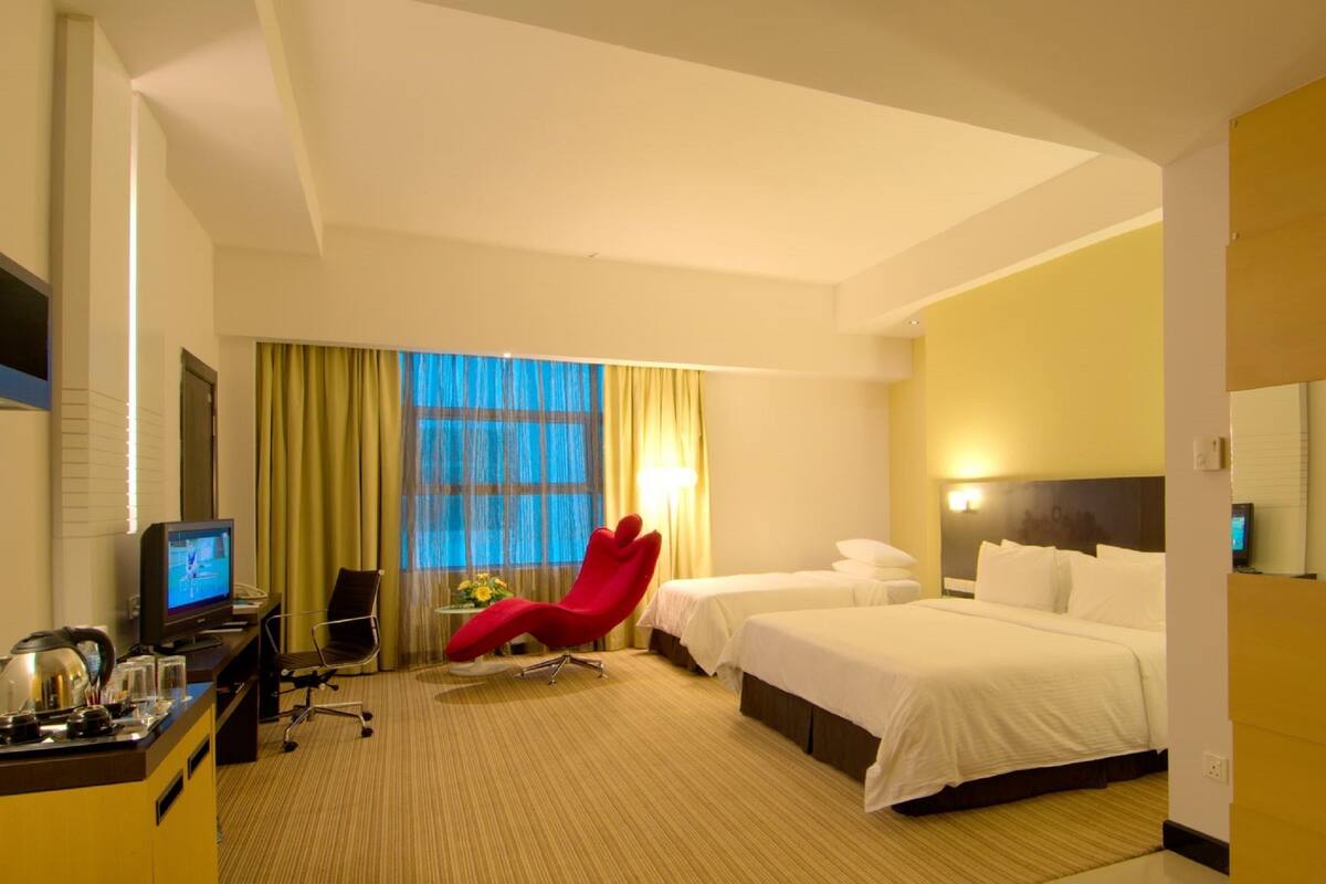 A hotel room with two beds, a desk with a computer, a red chair, and a TV.
