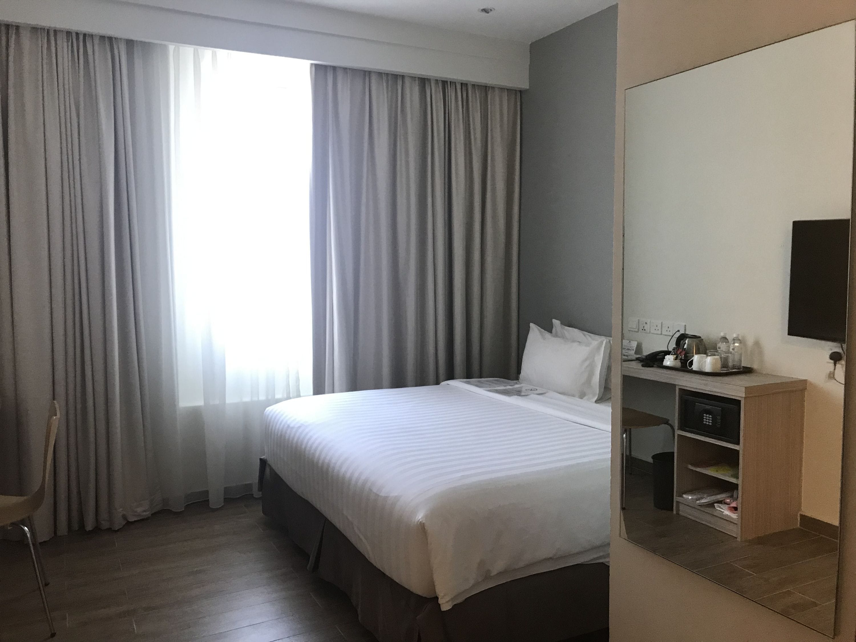 A hotel room with a large bed, a desk with a telephone and a coffee maker, and a television on the wall.
