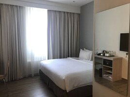 A hotel room with a large bed, a desk with a telephone and a coffee maker, and a television on the wall.
