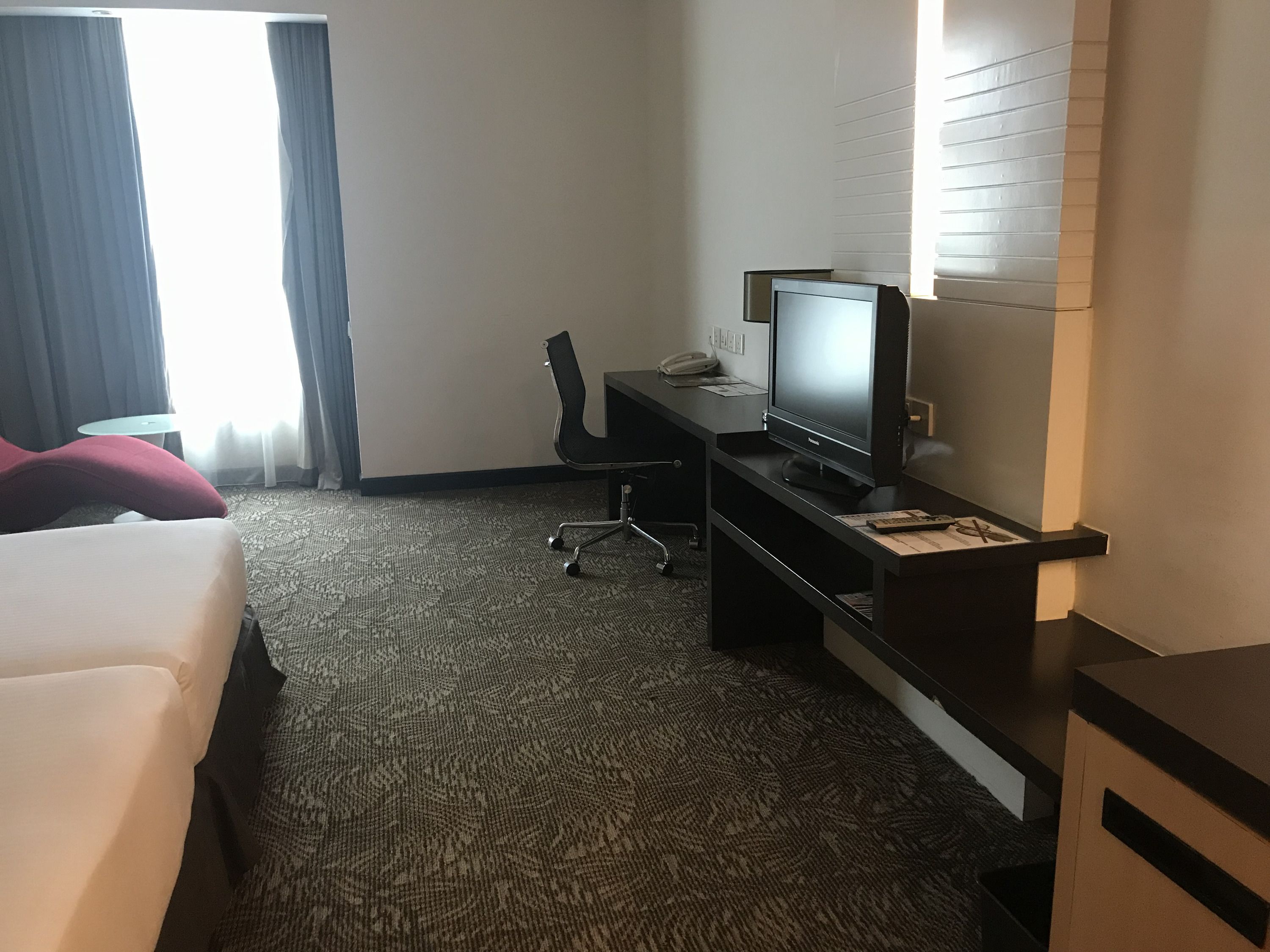 Ein Hotelzimmer mit einem Bett, einem Schreibtisch mit Computer, einem Sessel und einem Fernseher.