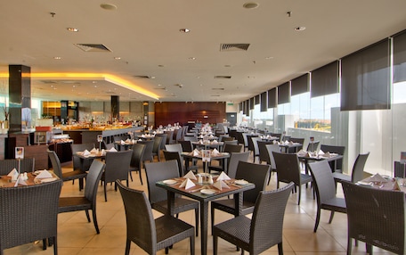 Un restaurante espacioso con numerosas mesas y sillas, una zona de bufé y amplias ventanas que dejan entrar mucha luz natural.