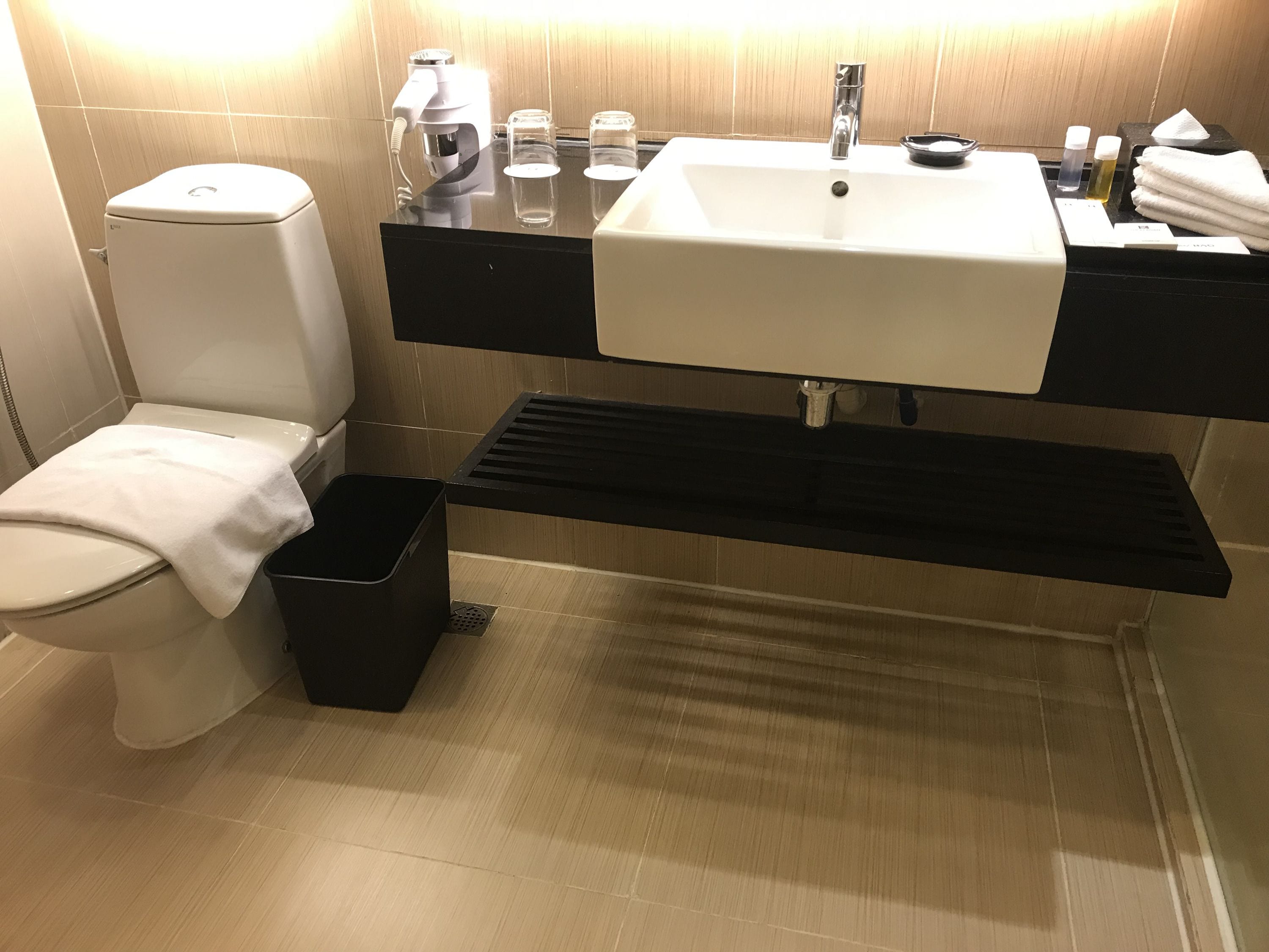 Une salle de bain moderne équipée de toilettes, d’un lavabo et d’une poubelle noire.