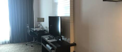 Een hotelkamer met een bureau, stoel, televisie en een groot raam met zonwering.
