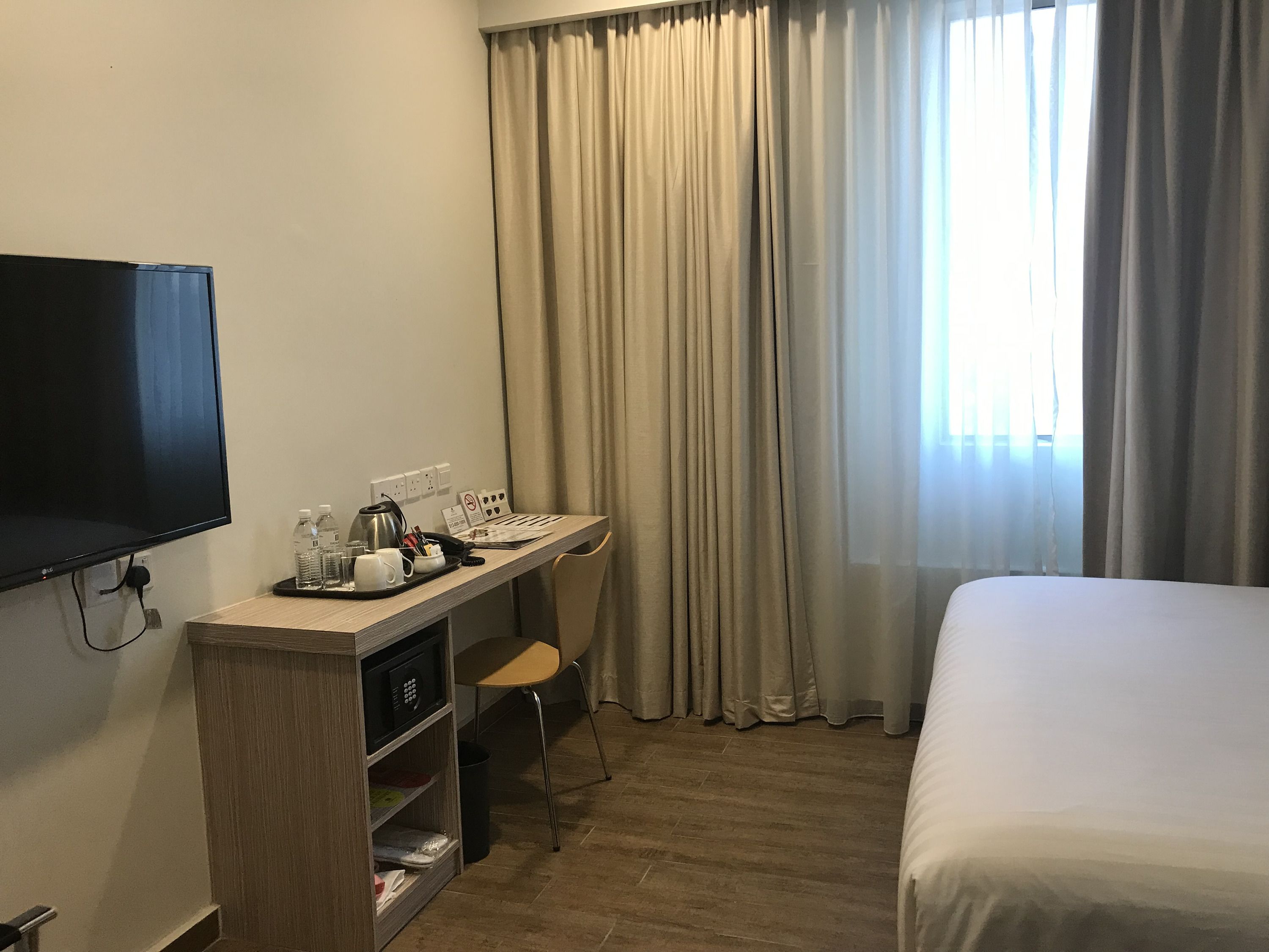 Ein Hotelzimmer mit Bett, Schreibtisch mit Computer, Fernseher und einem Fenster mit Vorhängen.