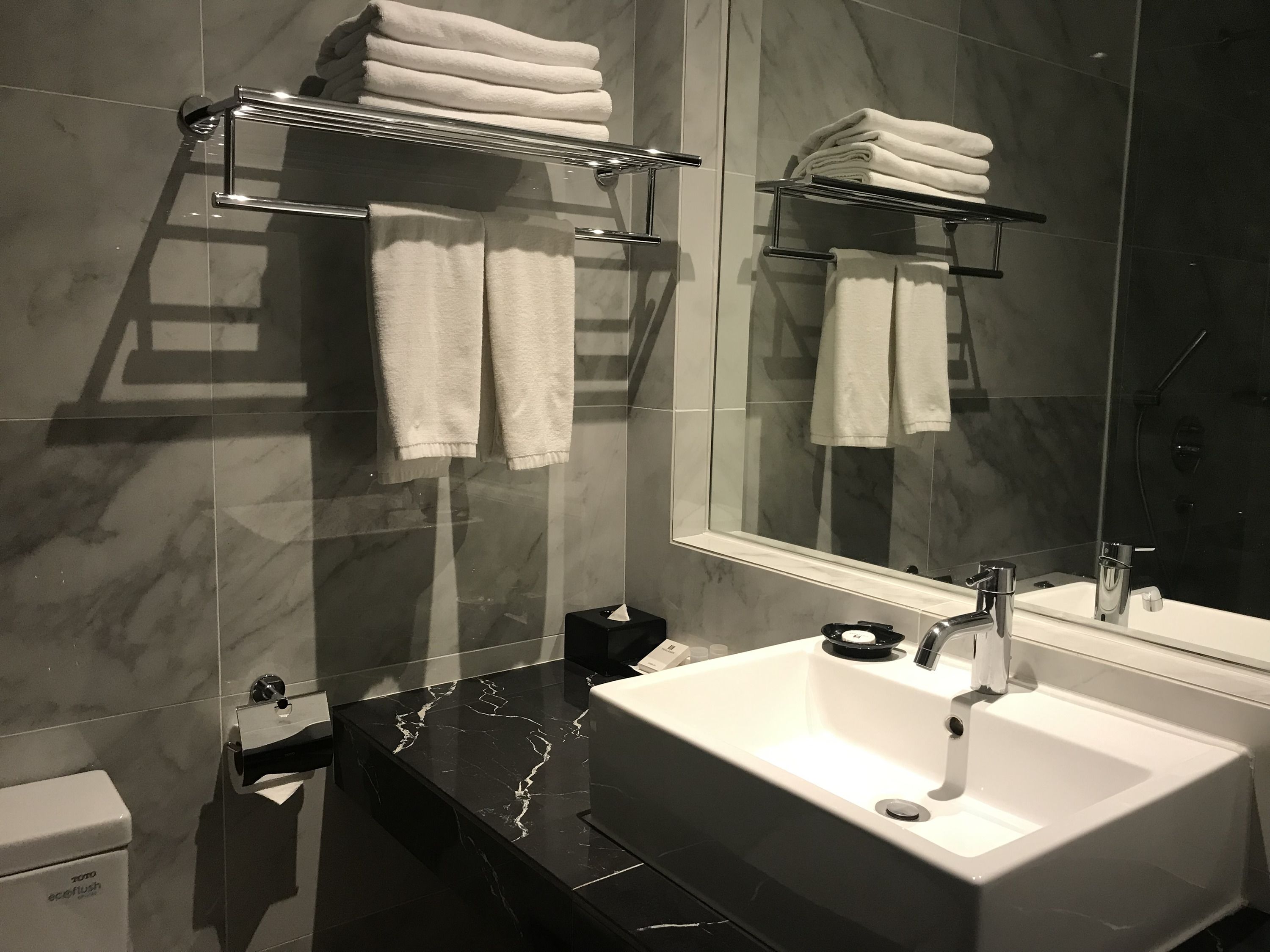 A modern bathroom with a large mirror, a white sink, and two towel racks.