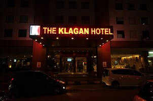 Exterior del Hotel Klagan, con un llamativo letrero iluminado, un estacionamiento y una moderna fachada.