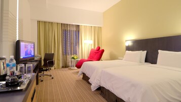 Et hotelværelse med en seng, et skrivebord med fjernsyn, en rød stol og et lille bord med en lampe.