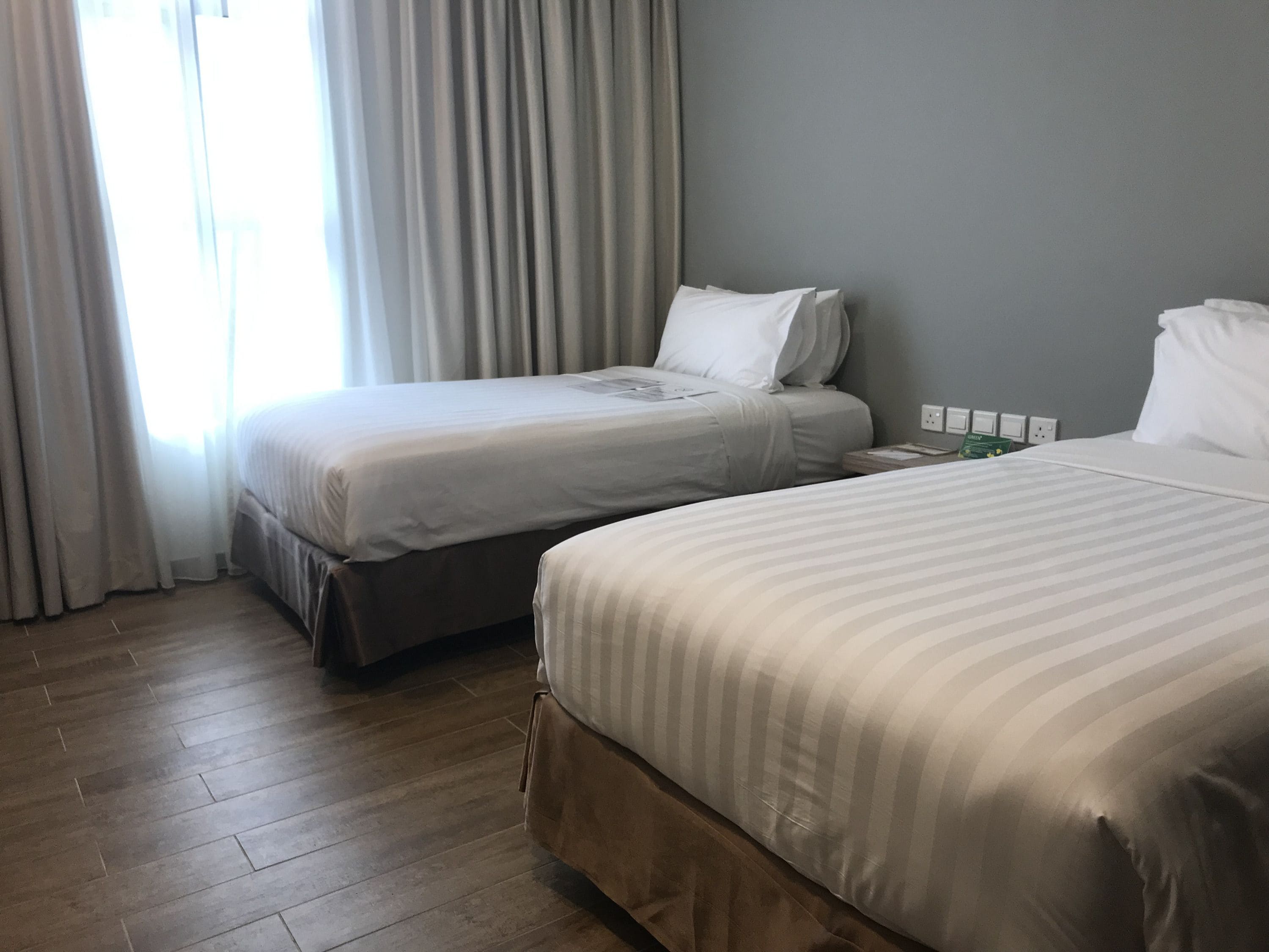 A hotel room with two beds, a wooden floor, and a window with curtains.