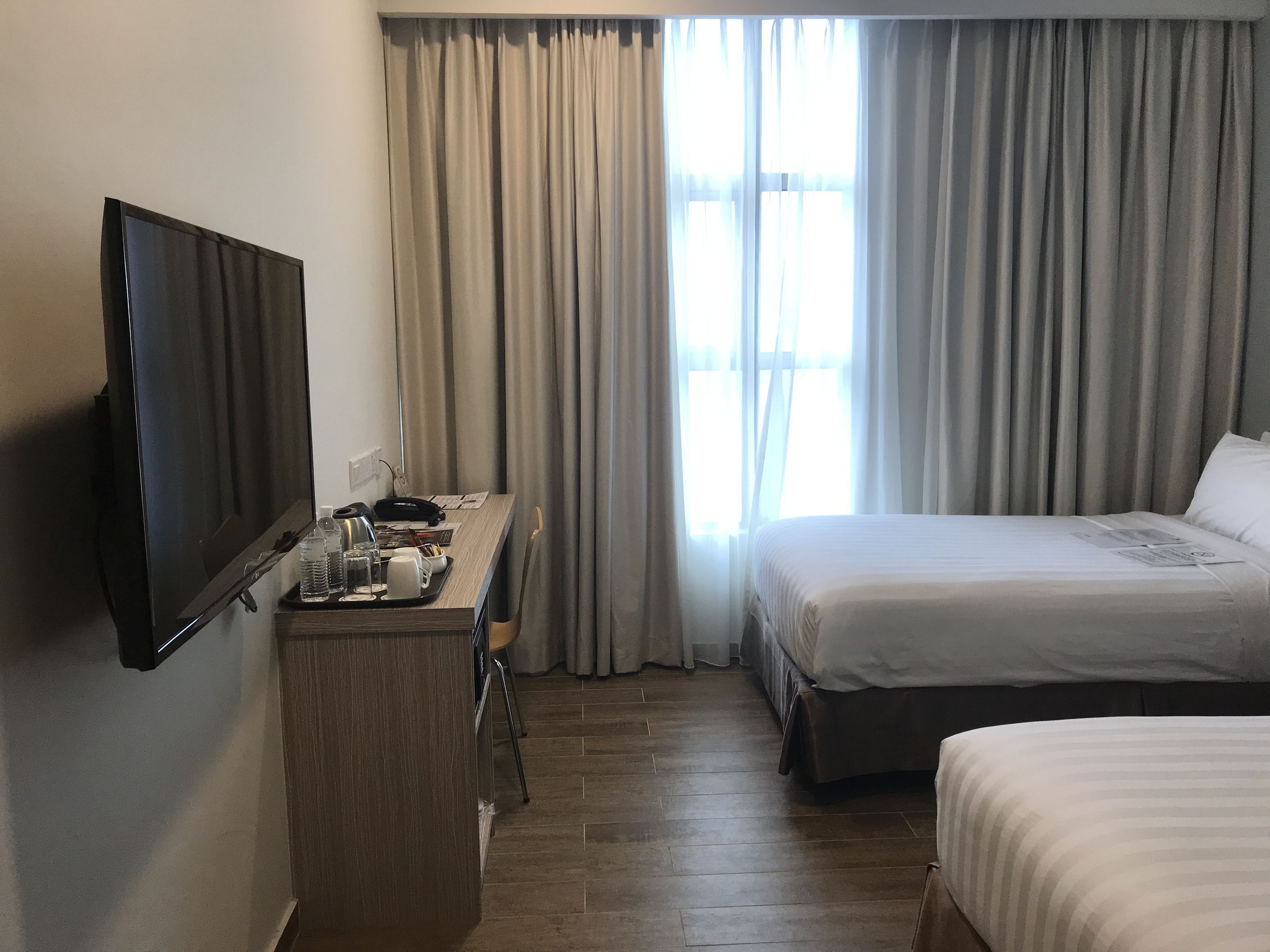 A hotel room with a bed, a desk with a television, and a window with curtains.
