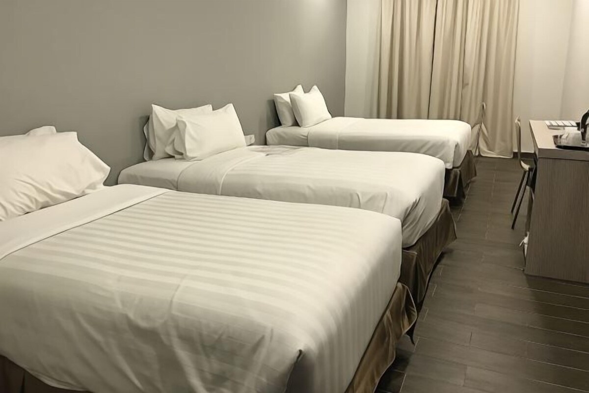 A hotel room with three beds arranged in a row, a desk, and a chair.