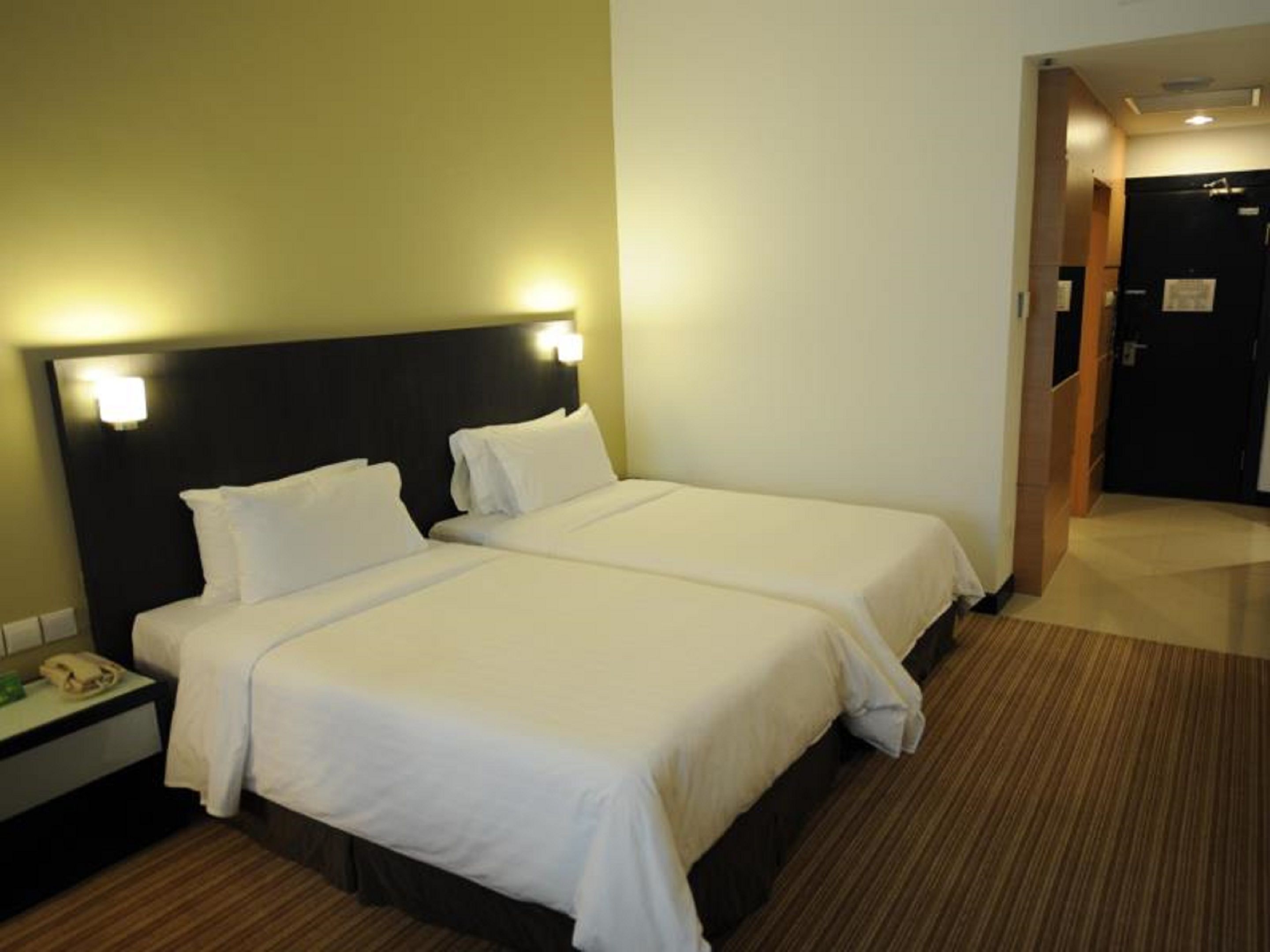 A hotel room with two beds, a bedside table with a phone, and a door leading to another room.