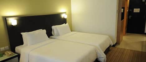 A hotel room with two beds, a bedside table with a phone, and a door leading to another room.