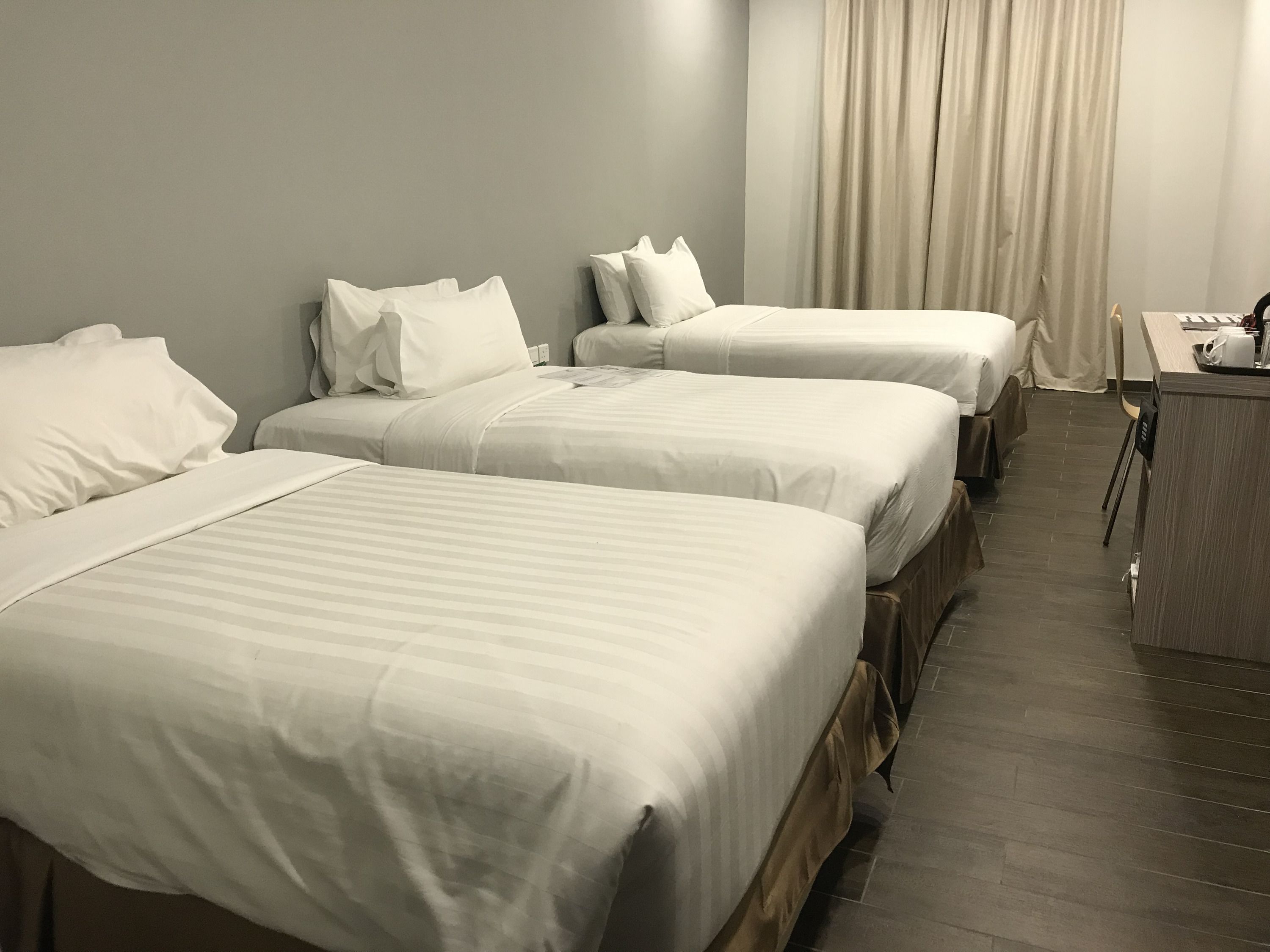 Een hotelkamer met drie enkele bedden, een bureau en een stoel.