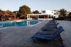 A swimming pool with lounge chairs and a modern building in the background. - Evita Elite (Rhodes)