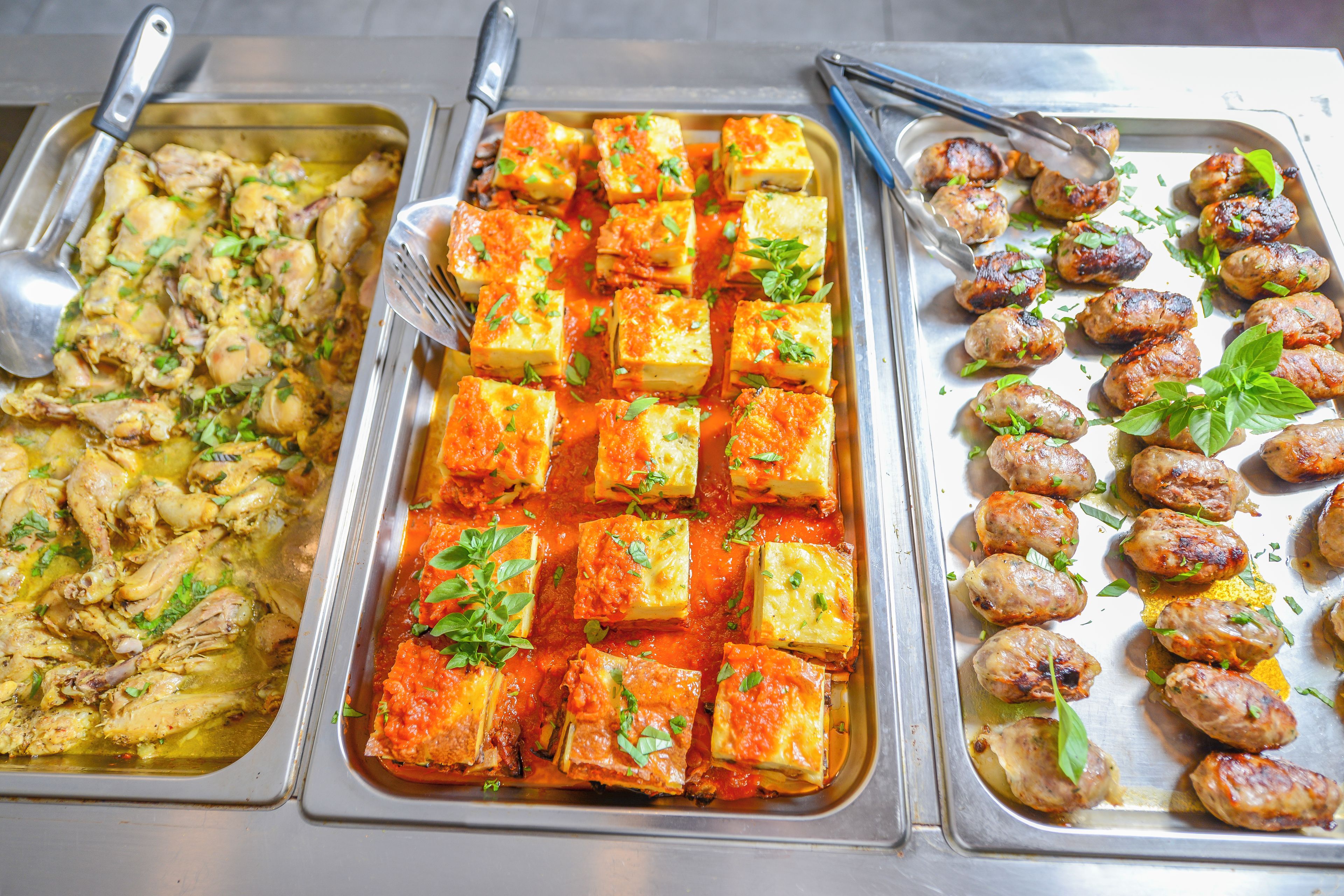 A buffet with various dishes including roasted chicken, paneer in tomato sauce, and grilled sausages.