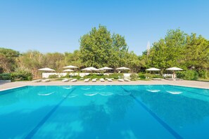 Piscina con sillas de descanso y sombrillas, rodeada de árboles.