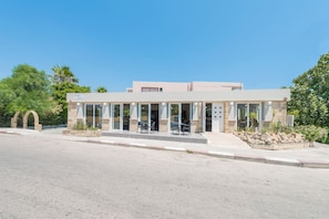 A modern building with a cafe area featuring outdoor seating, stone arches, and a clear sky.