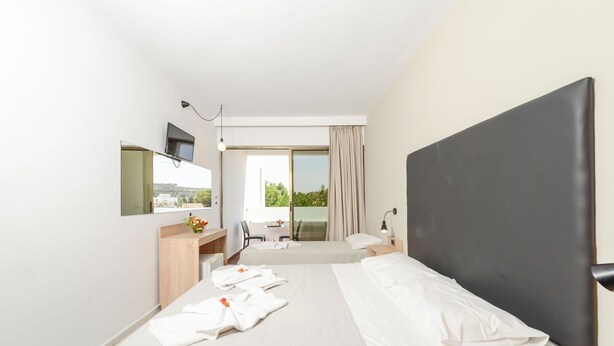 Une chambre d’hôtel moderne dotée d’un grand lit, d’un bureau avec une chaise, d’un téléviseur à écran plat fixé au mur et d’une grande fenêtre avec des rideaux.