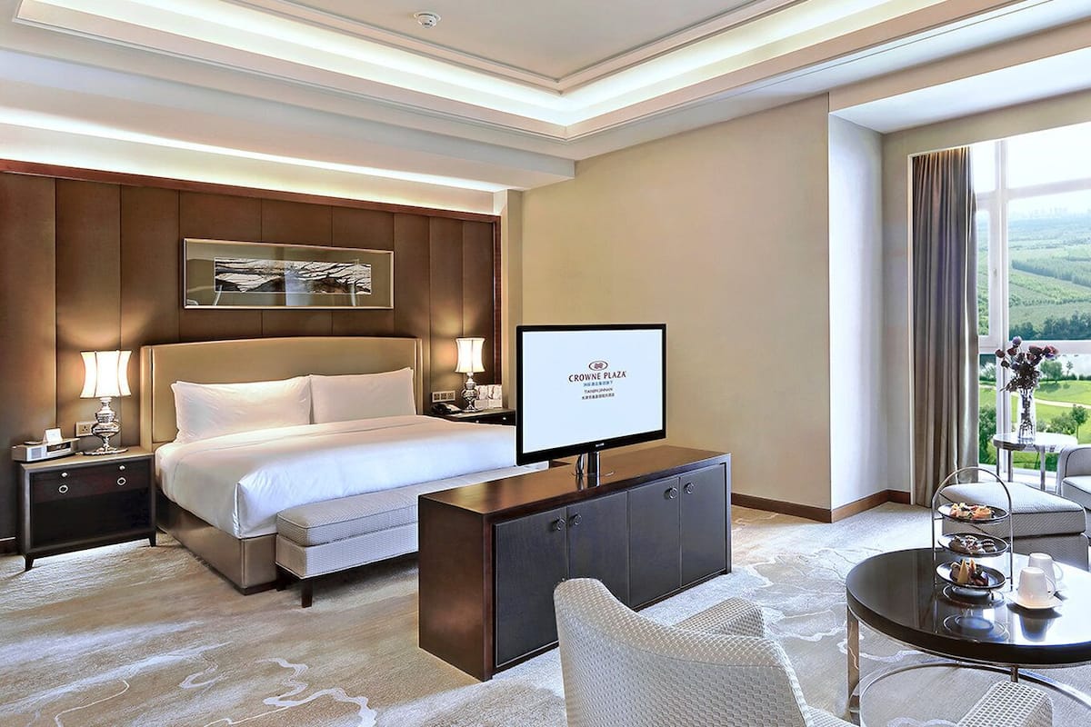 A hotel room with a bed, a TV, a desk, a chair, a coffee table, and a view of the outdoors.