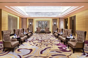Un hall d’hôtel doté d’un espace salon central, de plusieurs fauteuils, d’une moquette à motifs et d’un lustre.
