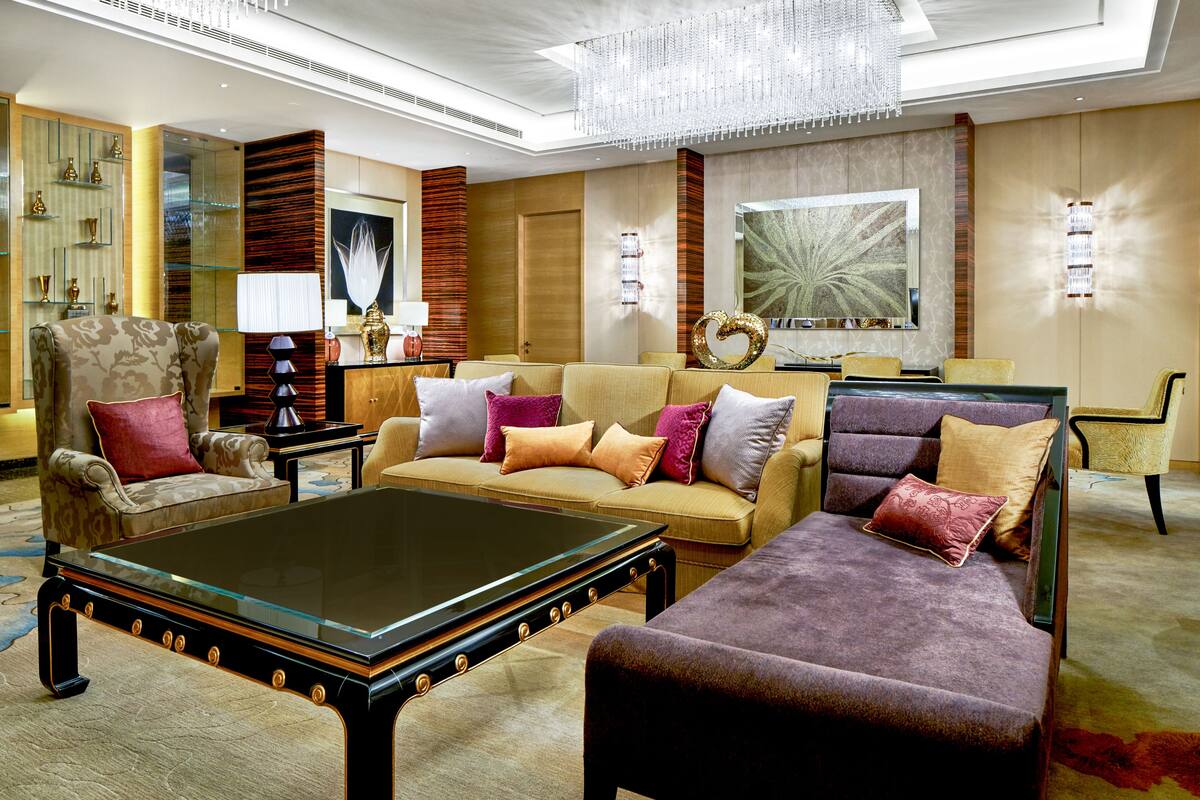 A spacious living room with a large sofa, armchairs, a glass coffee table, and a chandelier.