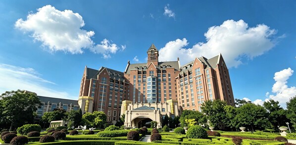 Un hotel grande e histórico con una torre central, rodeado de jardines cuidados y un cielo azul despejado.