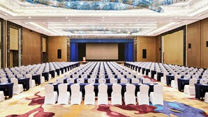 A conference room with rows of tables and chairs, a large screen at the front, and a chandelier overhead. - Crowne Plaza Tianjin Jinnan by IHG (Tianjin)