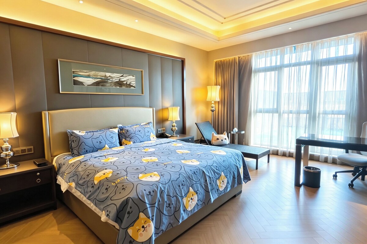 A hotel room with a large bed, two bedside tables with lamps, a desk with a chair, and a large window with curtains.