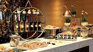 Montaje de bufé con diversos alimentos, una selección de vinos y plantas decorativas.