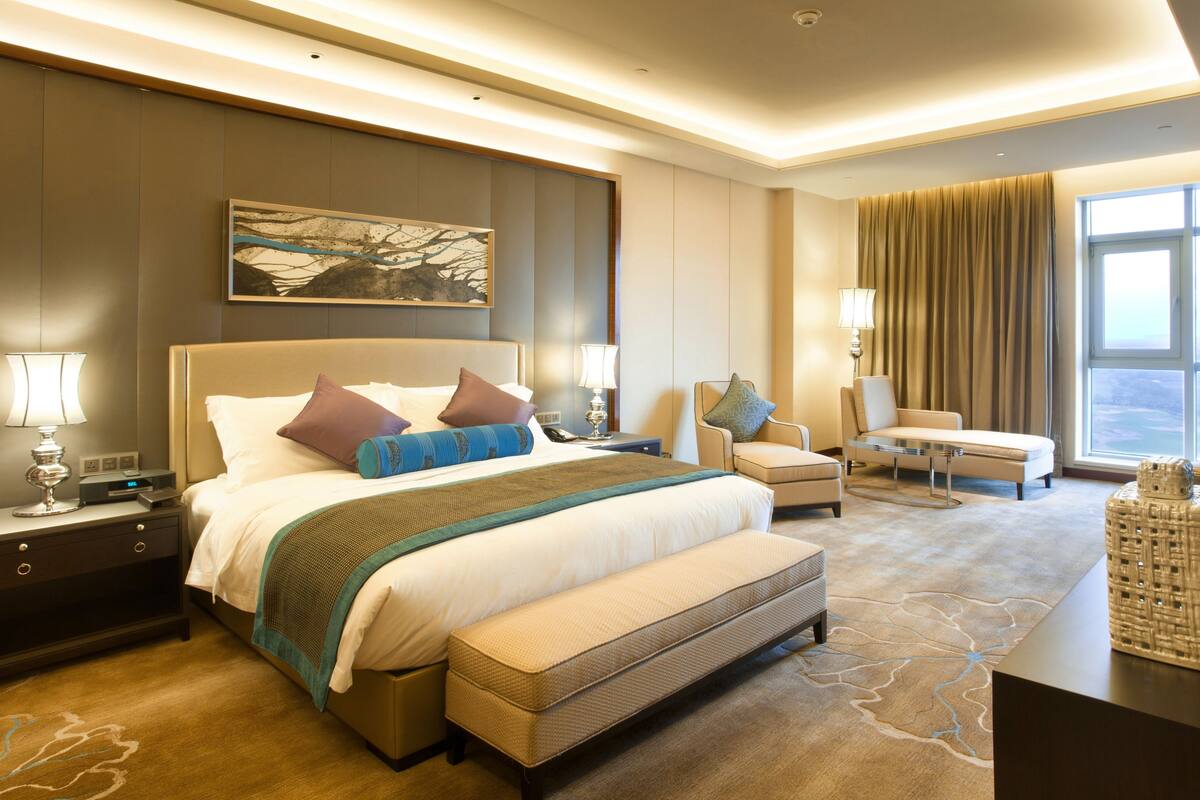 A modern hotel room with a large bed, a seating area, and a view of the outdoors.
