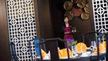 A restaurant interior with a waiter holding a tray, tables with orange napkins, and a decorative wall with circular patterns.
