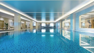 A large indoor swimming pool with a tiled floor and walls, surrounded by lounge areas and exercise equipment.