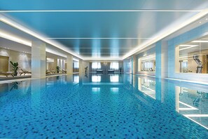 A large indoor swimming pool with a tiled floor and walls, surrounded by lounge areas and exercise equipment. - Crowne Plaza Tianjin Jinnan by IHG (Tianjin)