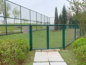 Un espacio exterior cercado con entrada pavimentada, rodeado de follaje y árboles.