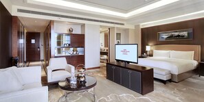 Habitación de hotel con cama, televisión, zona de estar con mesa y minibar.