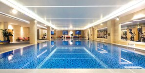 A large indoor swimming pool with a blue tiled floor, surrounded by lounge chairs and exercise equipment. - Crowne Plaza Tianjin Jinnan by IHG (Tianjin)