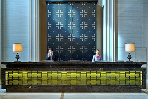A reception desk with two individuals seated behind it, a patterned backdrop, and a marble counter with a geometric design. - Crowne Plaza Tianjin Jinnan by IHG (Tianjin)