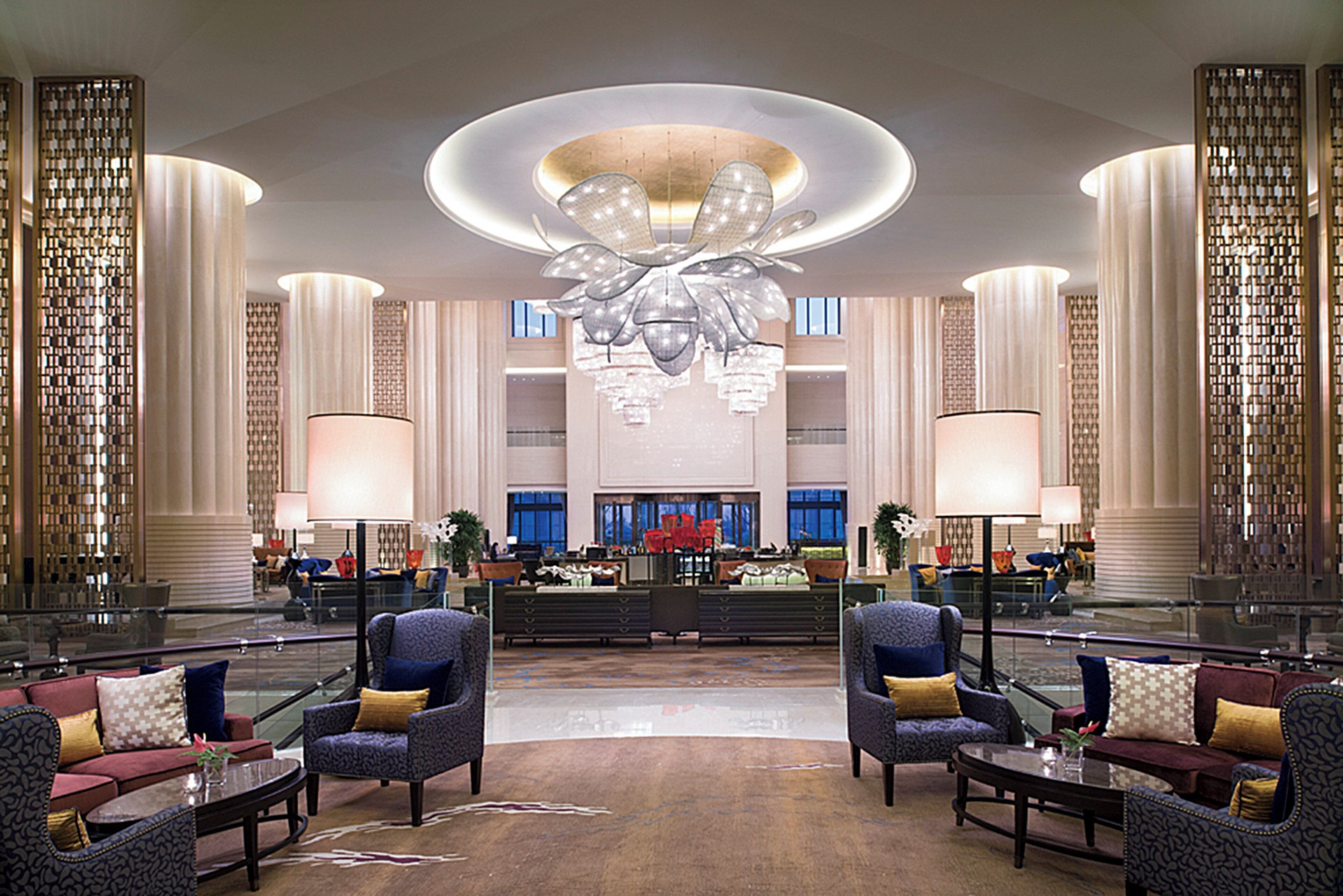 A spacious lobby with a central reception desk, multiple seating areas, and a large chandelier.