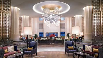 A spacious lobby with a central reception desk, multiple seating areas, and a large chandelier.